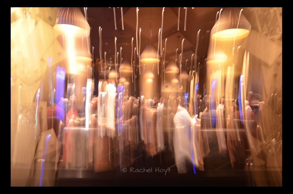ICM photo of a poker room with golden light streaks and shadows of large playing cards at the right and left sides.